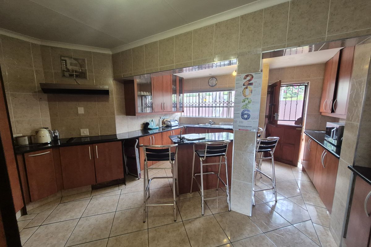 A functional kitchen featuring wood-finish cabinetry, dark countertops, a breakfast bar, and tiled flooring with direct access to the exterior.