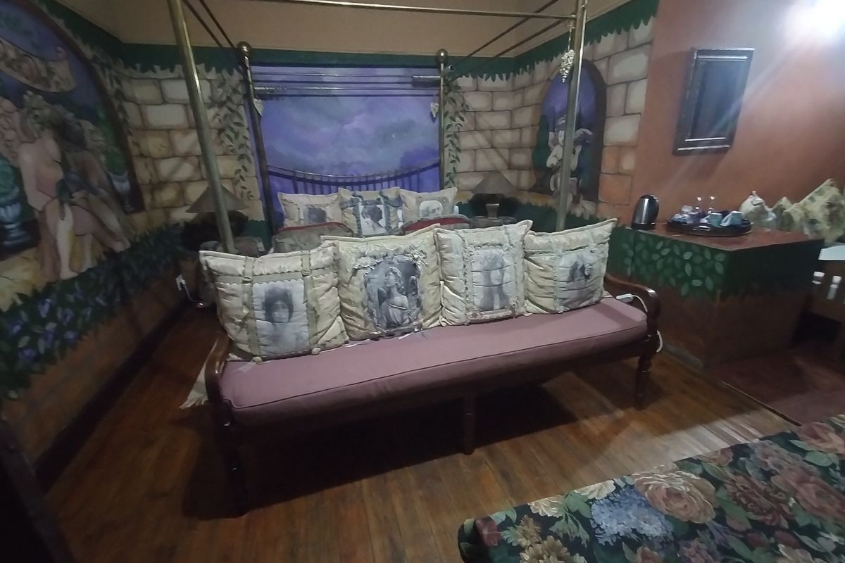A bedroom featuring hardwood flooring and a four-poster bed frame, characterized by unique mural-style wall finishes.