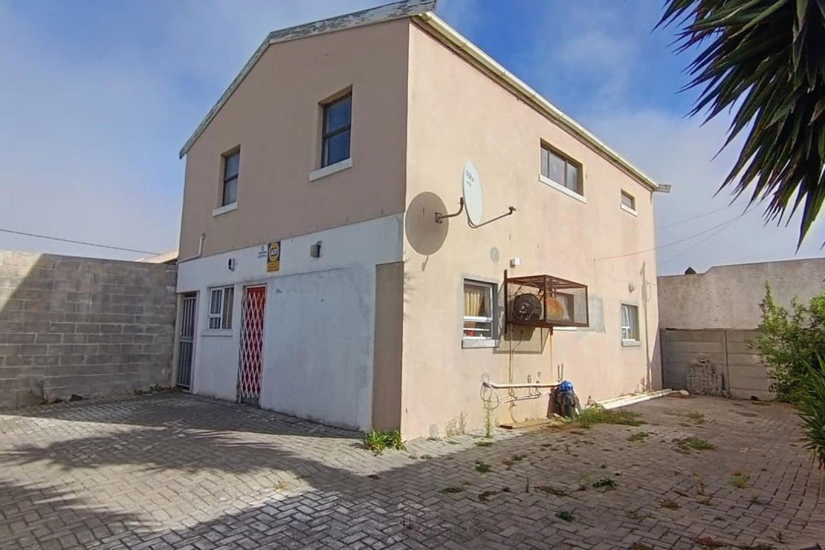Rear view of a two-story house featuring a paved courtyard, security gate, and concrete block boundary walls.