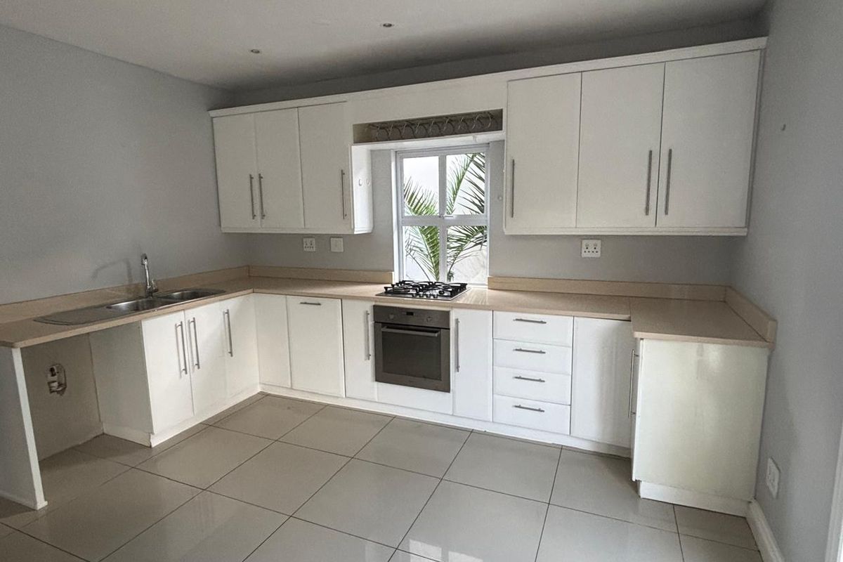 A clean, modern kitchen featuring white cabinetry, tiled flooring, a built-in oven, gas hob, and ample counter space.