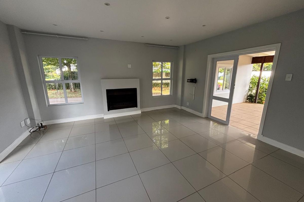 A bright, empty living room featuring large format floor tiles, a built-in fireplace, and direct access to an outdoor patio area.