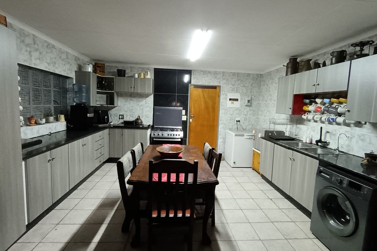 A functional kitchen featuring extensive built-in cabinetry, laminate countertops, a stainless steel sink, and a freestanding stove with tiled flooring throughout.