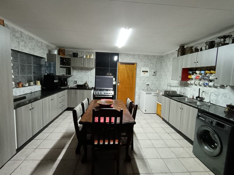 A functional kitchen featuring extensive built-in cabinetry, laminate countertops, a stainless steel sink, and a freestanding stove with tiled flooring throughout.