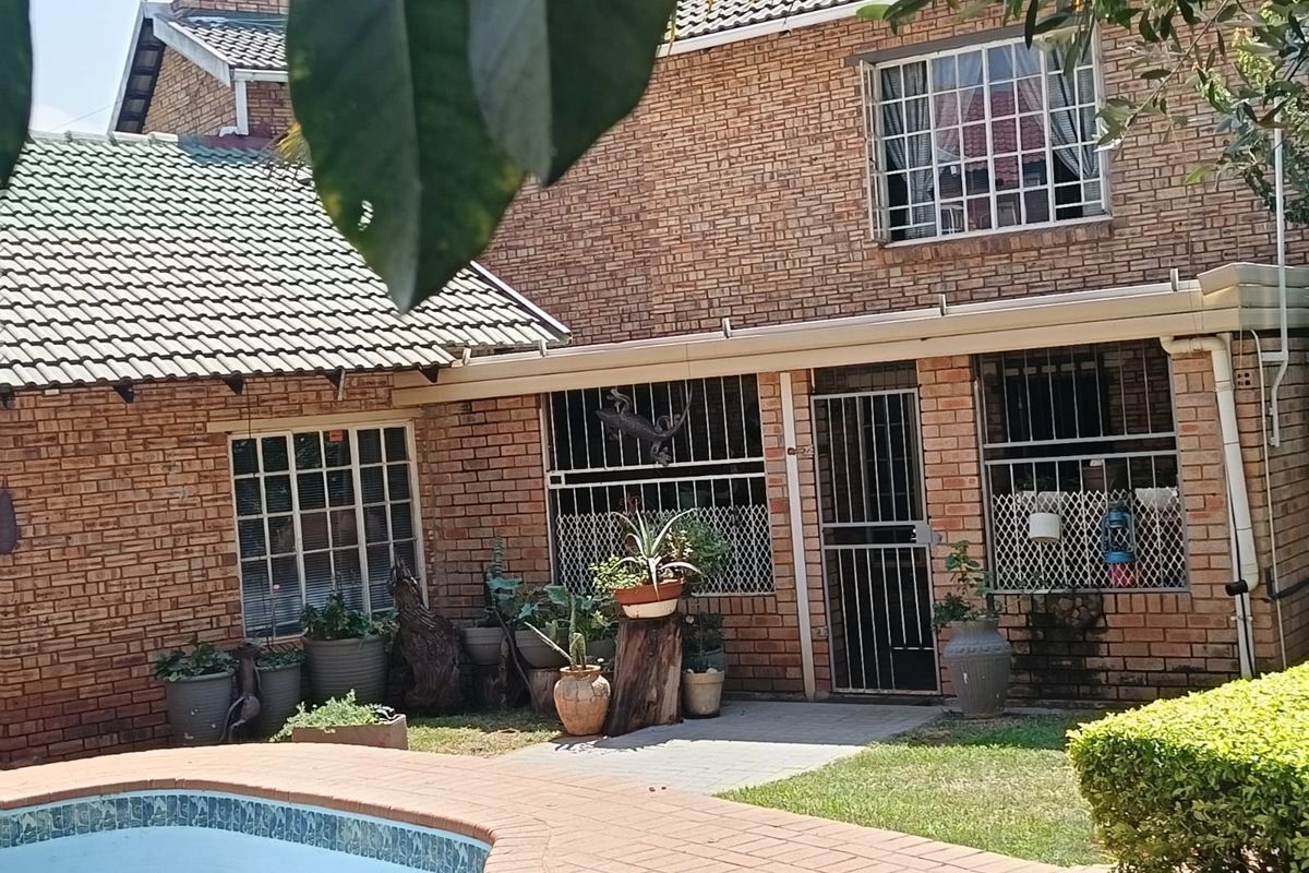 Rear view of a brick house featuring a swimming pool with paved surround, security bars on windows, and a security gate entrance.