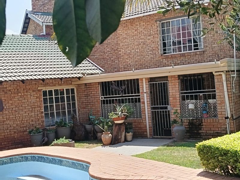 Rear view of a brick house featuring a swimming pool with paved surround, security bars on windows, and a security gate entrance.