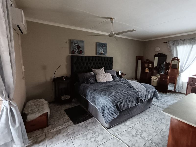 Spacious bedroom featuring tiled flooring, a ceiling fan, and a wall-mounted air conditioning unit.
