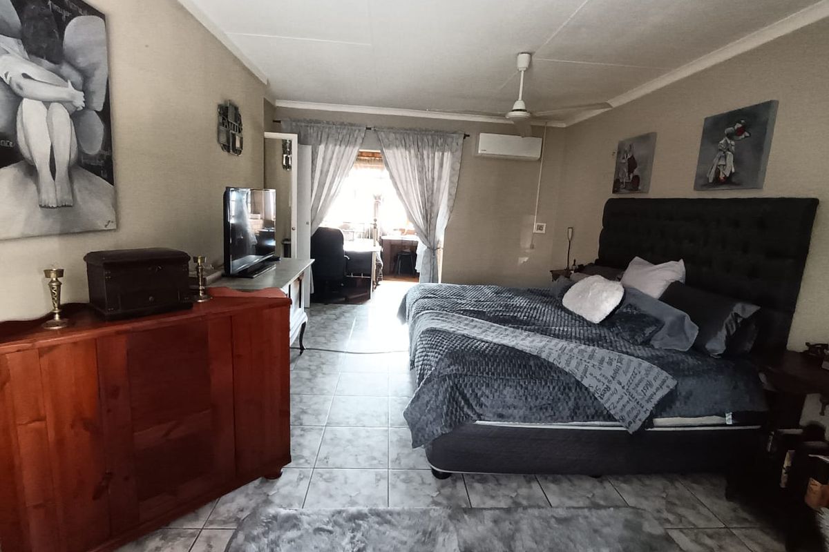 Spacious bedroom featuring tiled flooring, a ceiling fan, and a wall-mounted split-system air conditioner, with direct access to an adjoining space.