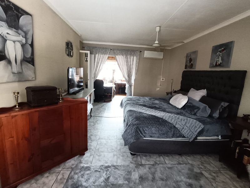 Spacious bedroom featuring tiled flooring, a ceiling fan, and a wall-mounted split-system air conditioner, with direct access to an adjoining space.