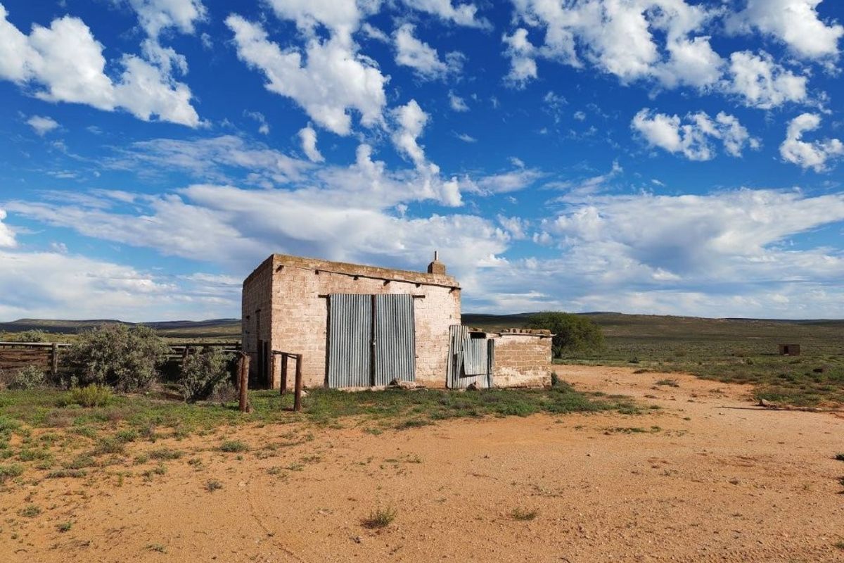 A rustic farm outbuilding featuring masonry walls and corrugated metal doors, situated in an open rural landscape.