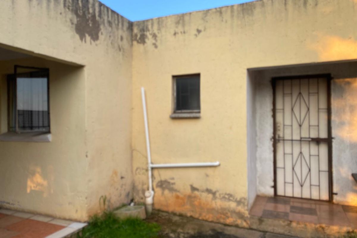 Rear exterior view of the property showing a tiled patio area, security gate, and visible signs of wall surface deterioration and damp staining.
