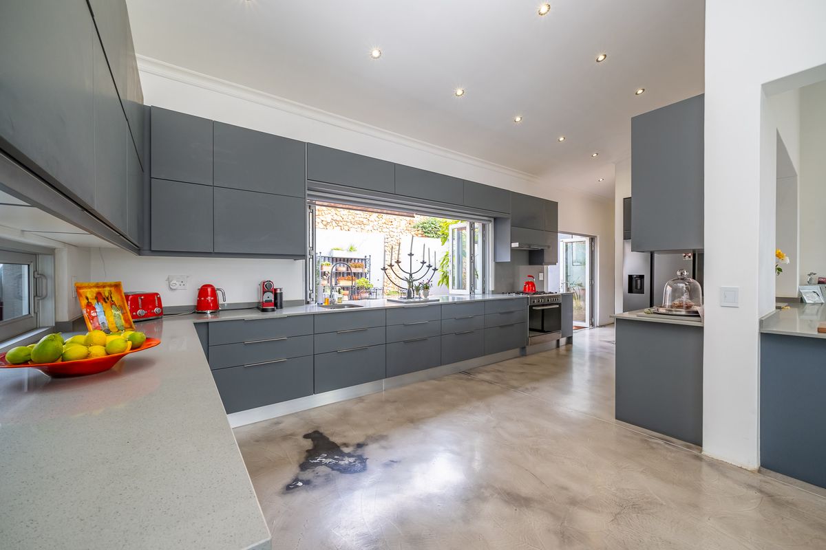 Modern kitchen featuring sleek grey cabinetry, stone countertops, polished concrete floors, and a convenient bi-fold window opening to the outdoor area.