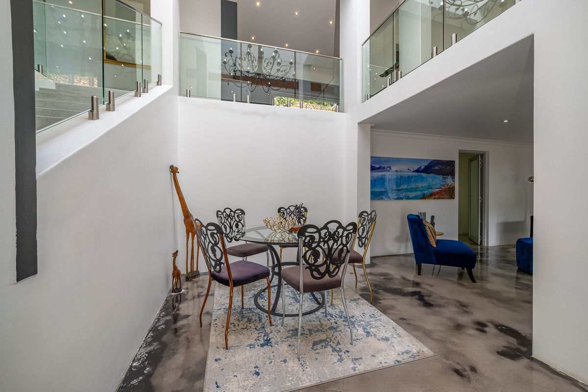 A bright, double-volume living area featuring polished concrete floors, a modern glass balustrade, and an open-plan layout connecting to the upper level.