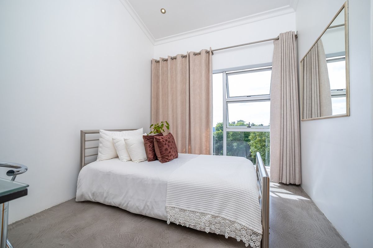 A bright bedroom featuring a vaulted ceiling, recessed lighting, and a large window with neutral curtains, offering a clean and modern living space.
