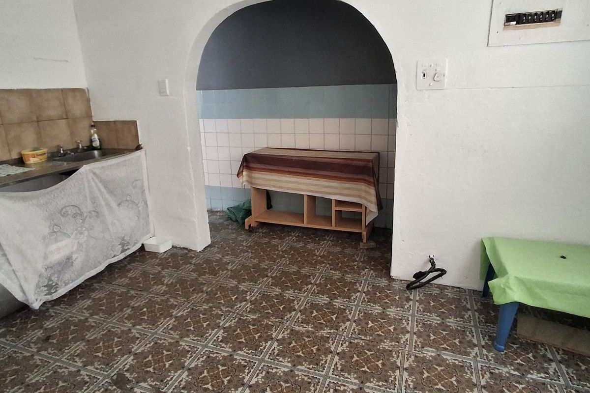 A dated kitchen area featuring patterned floor tiles, a built-in sink unit, and an arched transition to an adjacent utility space.