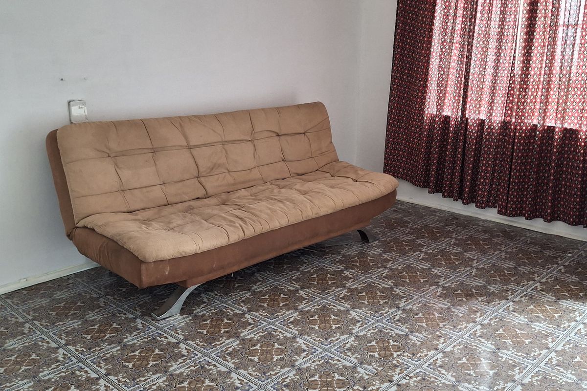 A living room featuring patterned ceramic floor tiles and a large window with traditional curtains.