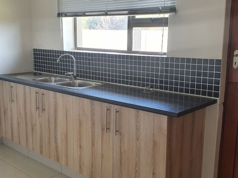 A clean, functional kitchen area featuring light wood-look cabinetry, a dark laminate countertop, a stainless steel double sink, and a tiled splashback.