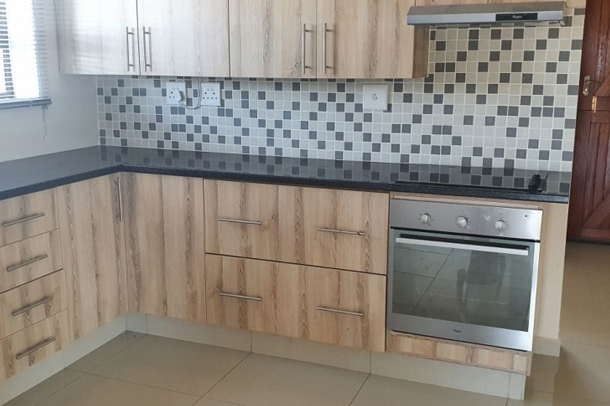 A clean, functional kitchen featuring light wood-grain cabinetry, dark granite countertops, a mosaic tile backsplash, and integrated stainless steel oven and extractor fan.