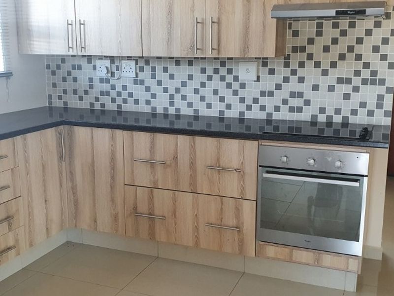 A clean, functional kitchen featuring light wood-grain cabinetry, dark granite countertops, a mosaic tile backsplash, and integrated stainless steel oven and extractor fan.