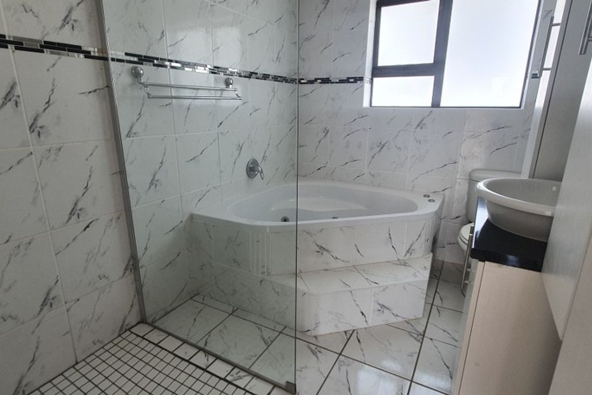 A clean bathroom featuring a corner bathtub, glass shower screen, tiled finishes, and a vanity basin.