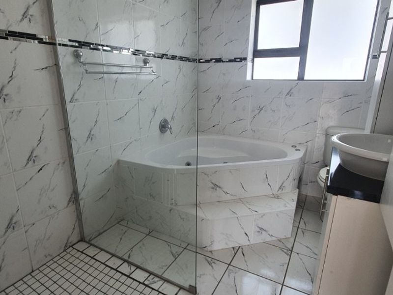 A clean bathroom featuring a corner bathtub, glass shower screen, tiled finishes, and a vanity basin.