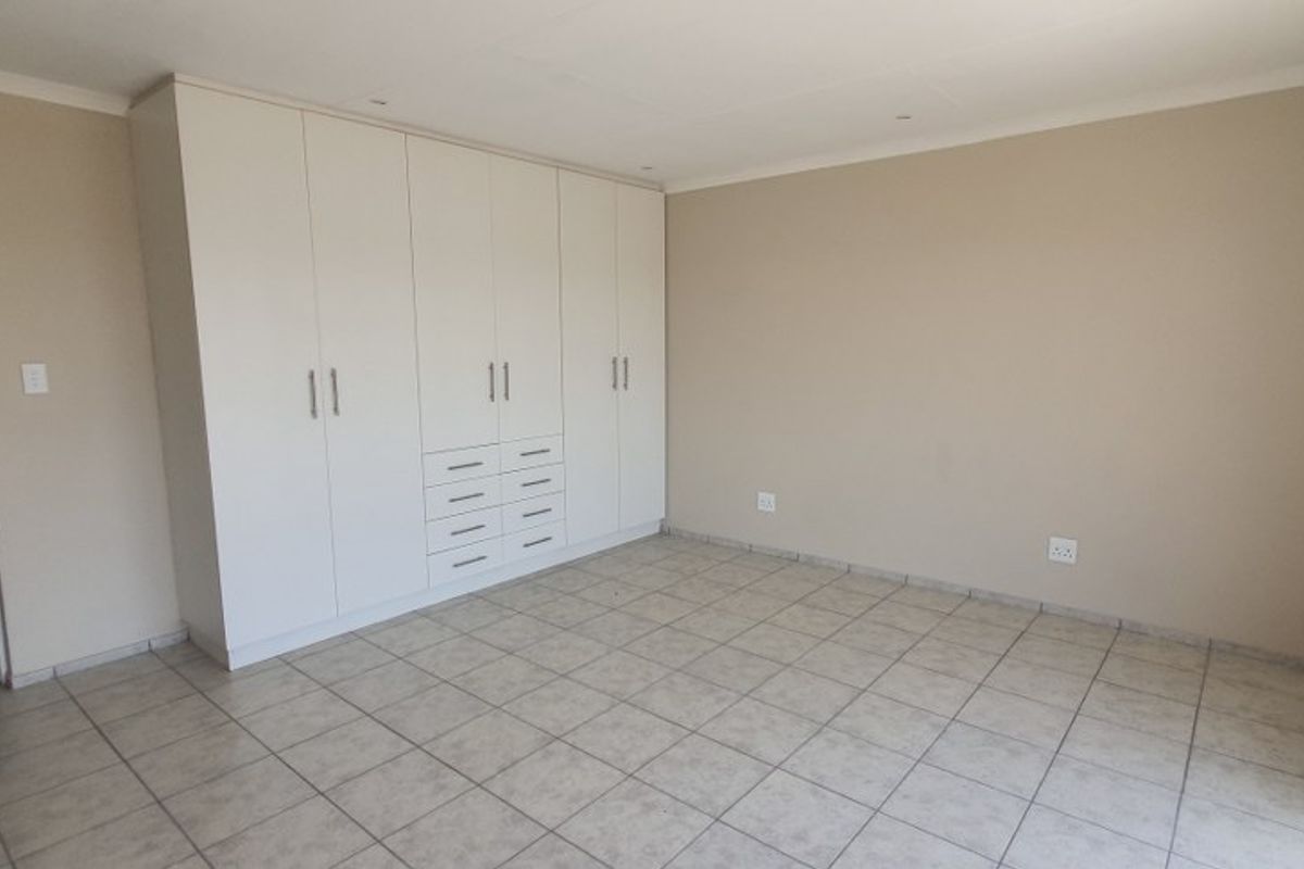 A spacious, empty bedroom featuring neutral wall tones, tiled flooring, and extensive built-in cupboard storage.