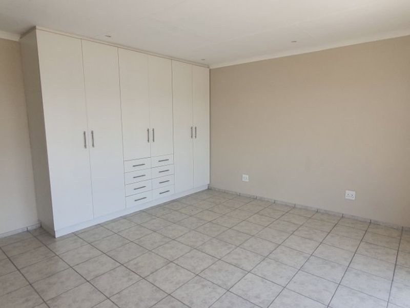 A spacious, empty bedroom featuring neutral wall tones, tiled flooring, and extensive built-in cupboard storage.