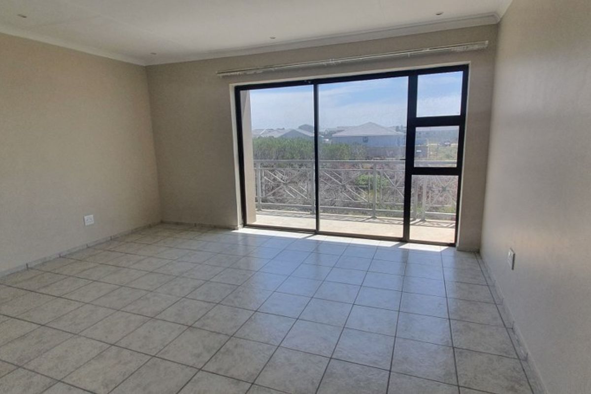 An empty, tiled living area featuring large sliding glass doors that provide natural light and direct access to an outdoor balcony.