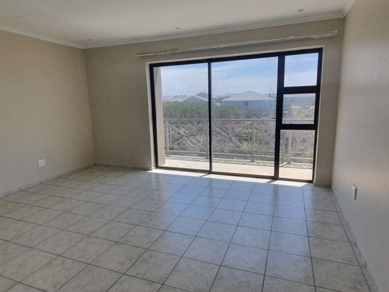 An empty, tiled living area featuring large sliding glass doors that provide natural light and direct access to an outdoor balcony.