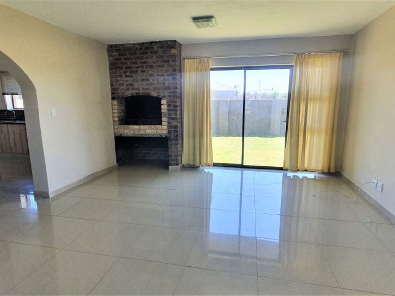 Spacious open-plan living area featuring a brick fireplace, tiled flooring, and direct access to the garden through sliding glass doors.