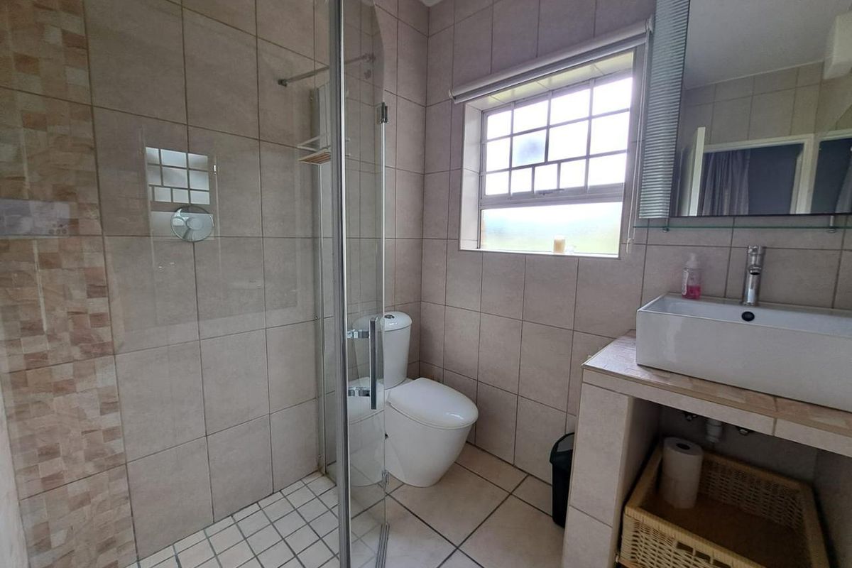 A functional bathroom featuring a glass-enclosed shower, a modern vessel sink on a tiled vanity, and a toilet.
