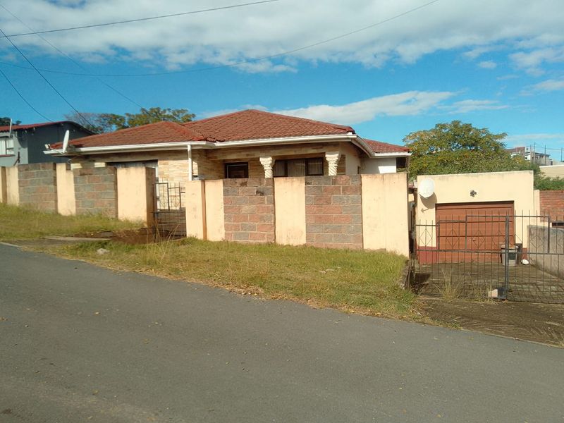 Front view of a single-story house featuring a tiled roof, stone cladding accents, and a secure brick boundary wall with an attached garage.