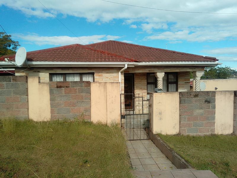 Front elevation of a single-story house featuring stone cladding, a tiled roof, decorative columns, and a gated entrance with a paved walkway.