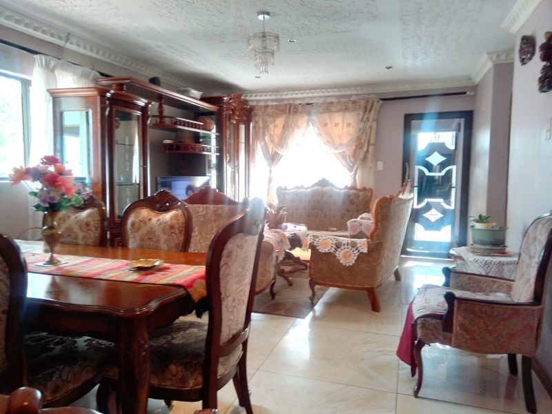 A spacious living area featuring polished tiled flooring, decorative ceiling molding, and an ornate ceiling rose, providing a traditional aesthetic.