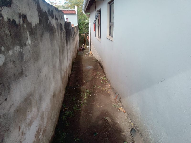 A narrow side passage between the house exterior wall and a boundary wall, showing signs of weathering and lack of maintenance.