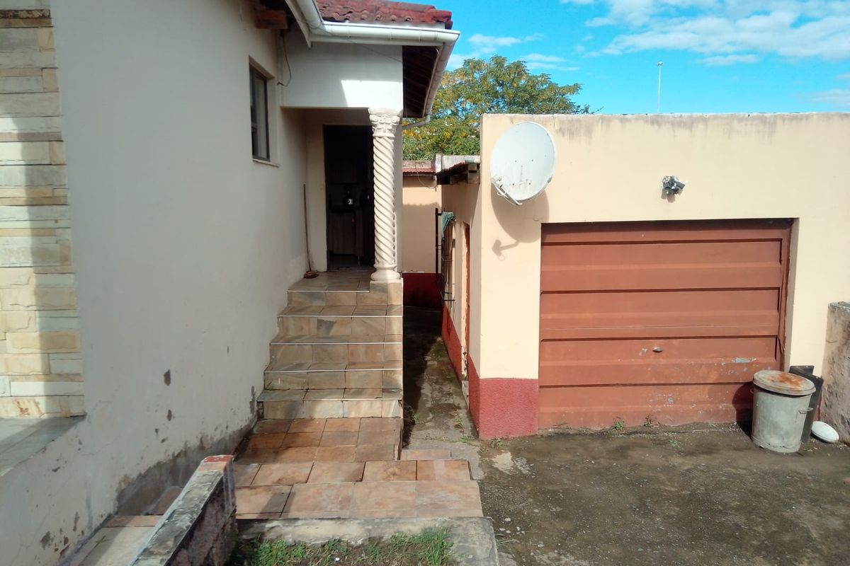 Rear exterior view showing a tiled staircase leading to an entrance, adjacent to a garage with a manual door and satellite dish installation.