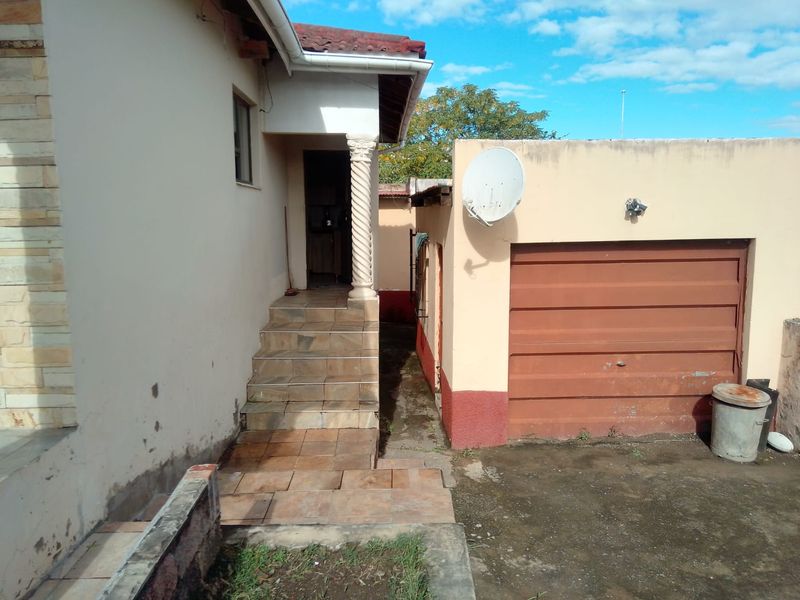 Rear exterior view showing a tiled staircase leading to an entrance, adjacent to a garage with a manual door and satellite dish installation.
