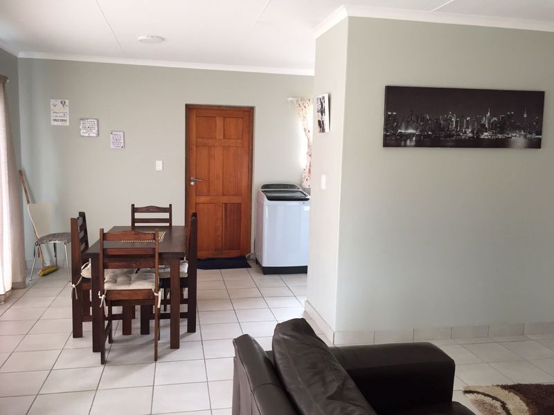 Open plan living and dining area featuring neutral wall tones, ceramic floor tiles, and a solid timber door leading to an adjacent utility space.