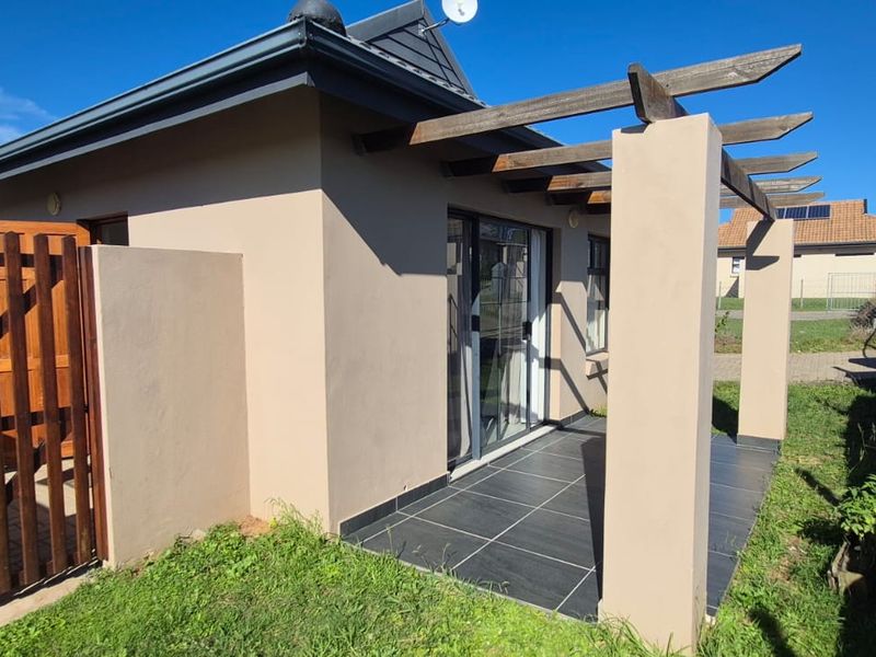A covered patio area featuring a timber pergola, tiled flooring, and a sliding glass door entrance, adjacent to a small garden and retaining wall.