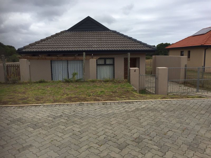 Front exterior view of a single-story house featuring a tiled roof, paved driveway, and gated entrance with boundary walling.