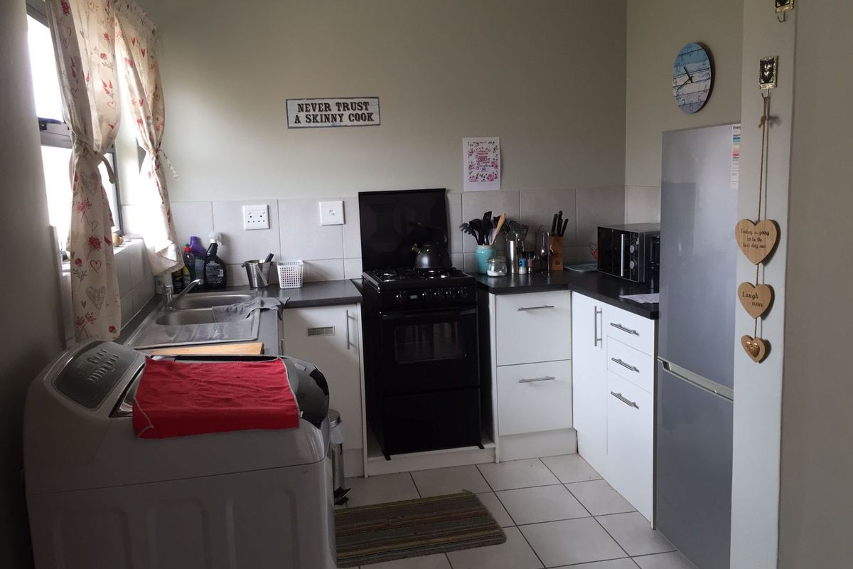 A functional kitchen featuring white cabinetry, laminate countertops, a tiled splashback, and a freestanding gas stove with ceramic floor tiles.