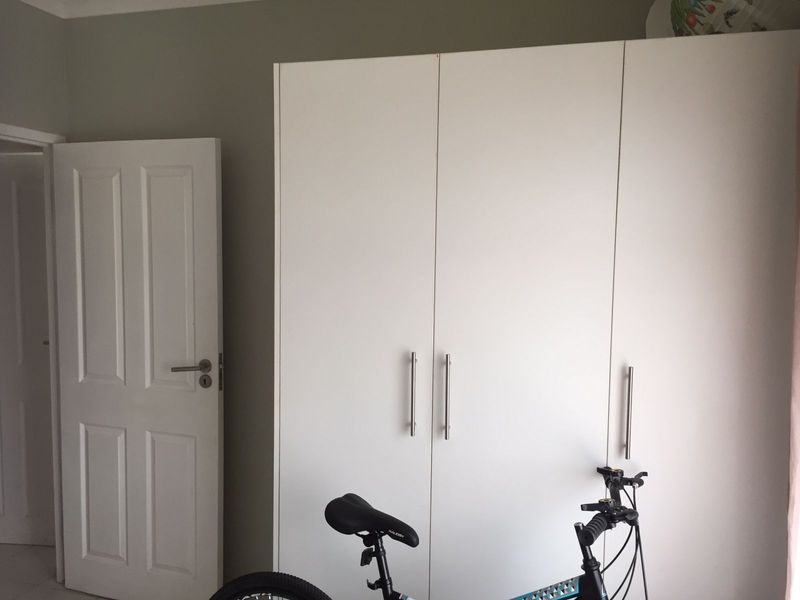 A bedroom featuring a modern white built-in wardrobe with sleek metal handles and a standard internal door.