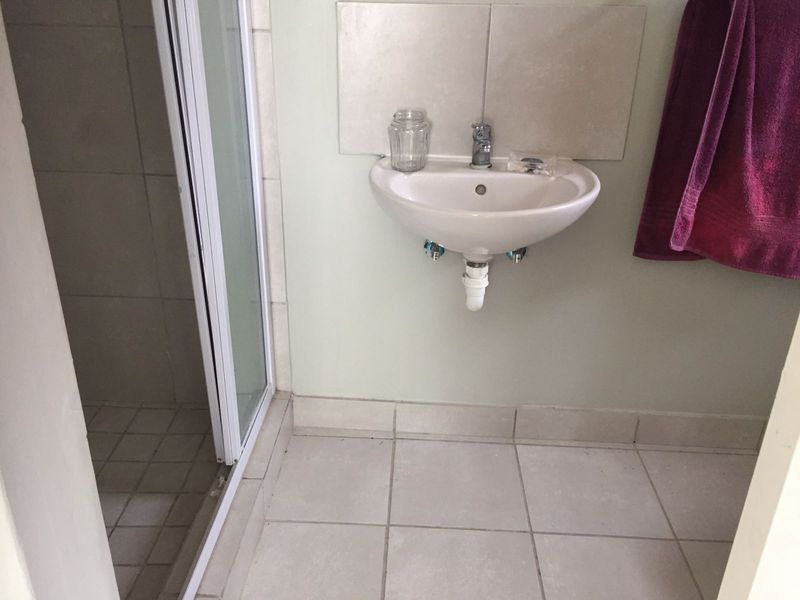 A compact bathroom featuring a wall-mounted basin with tiled splashback and a separate shower enclosure with tiled flooring.