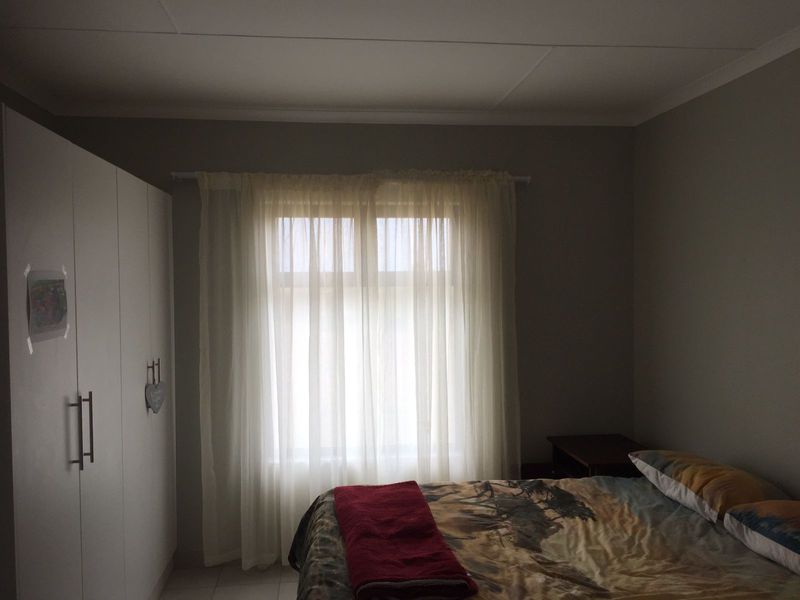 A bedroom featuring a built-in wardrobe and a window with sheer curtains, providing natural light to the space.