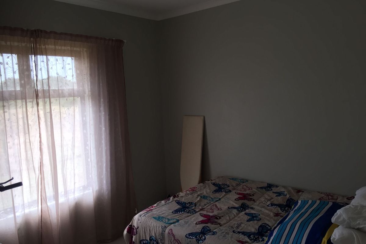 A standard bedroom featuring neutral wall paint, cove cornicing, and a window with sheer curtains.