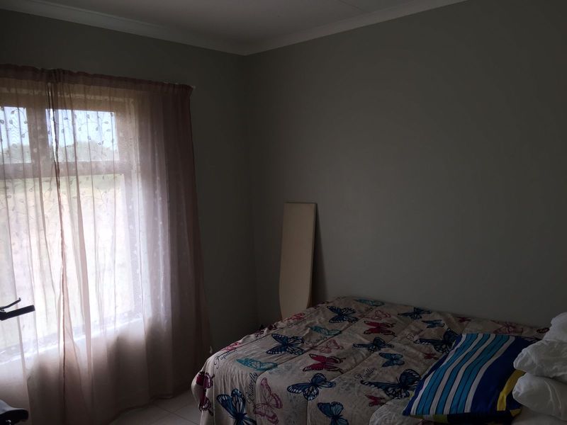 A standard bedroom featuring neutral wall paint, cove cornicing, and a window with sheer curtains.