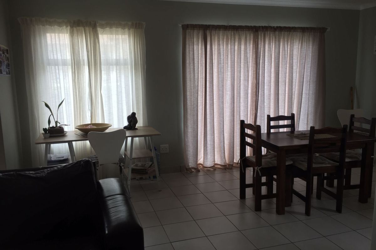 A living and dining area featuring neutral tiled flooring, large windows, and a sliding glass door providing natural light.