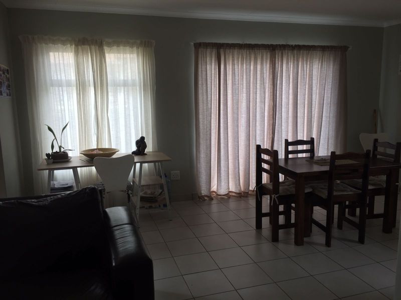 A living and dining area featuring neutral tiled flooring, large windows, and a sliding glass door providing natural light.