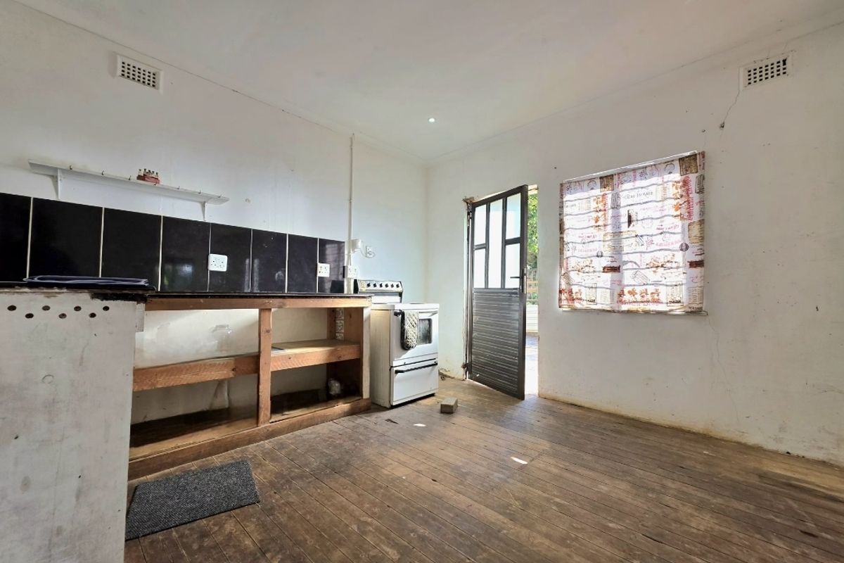 A basic kitchen area featuring timber flooring, a freestanding stove, and tiled splashback, requiring renovation to modernize the space.