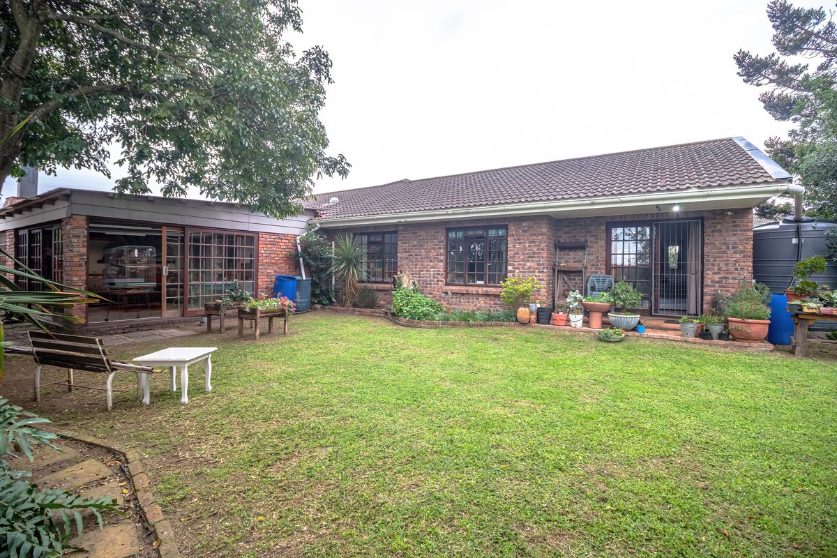 A rear view of the house featuring a brick facade, tiled roof, and a spacious lawn area with established garden beds.