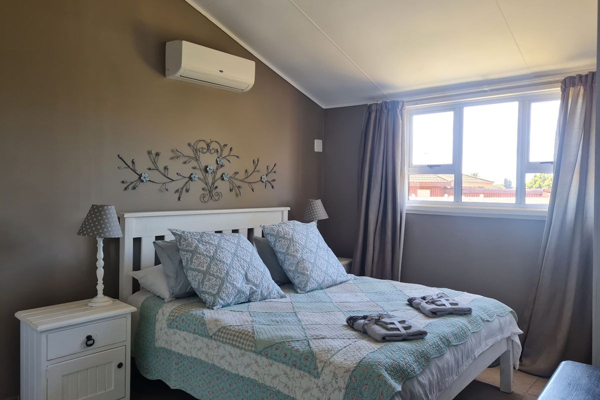 A bedroom featuring a raked ceiling, wall-mounted air conditioning unit, and large window providing natural light.